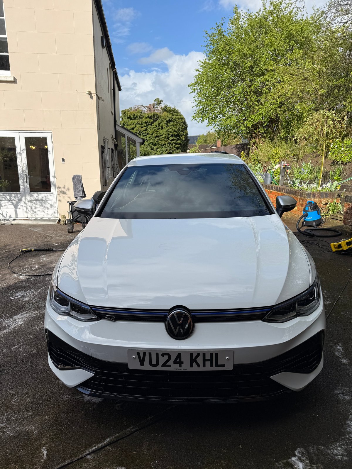 White Volkswagen car with black trim parked on driveway in front of beige house