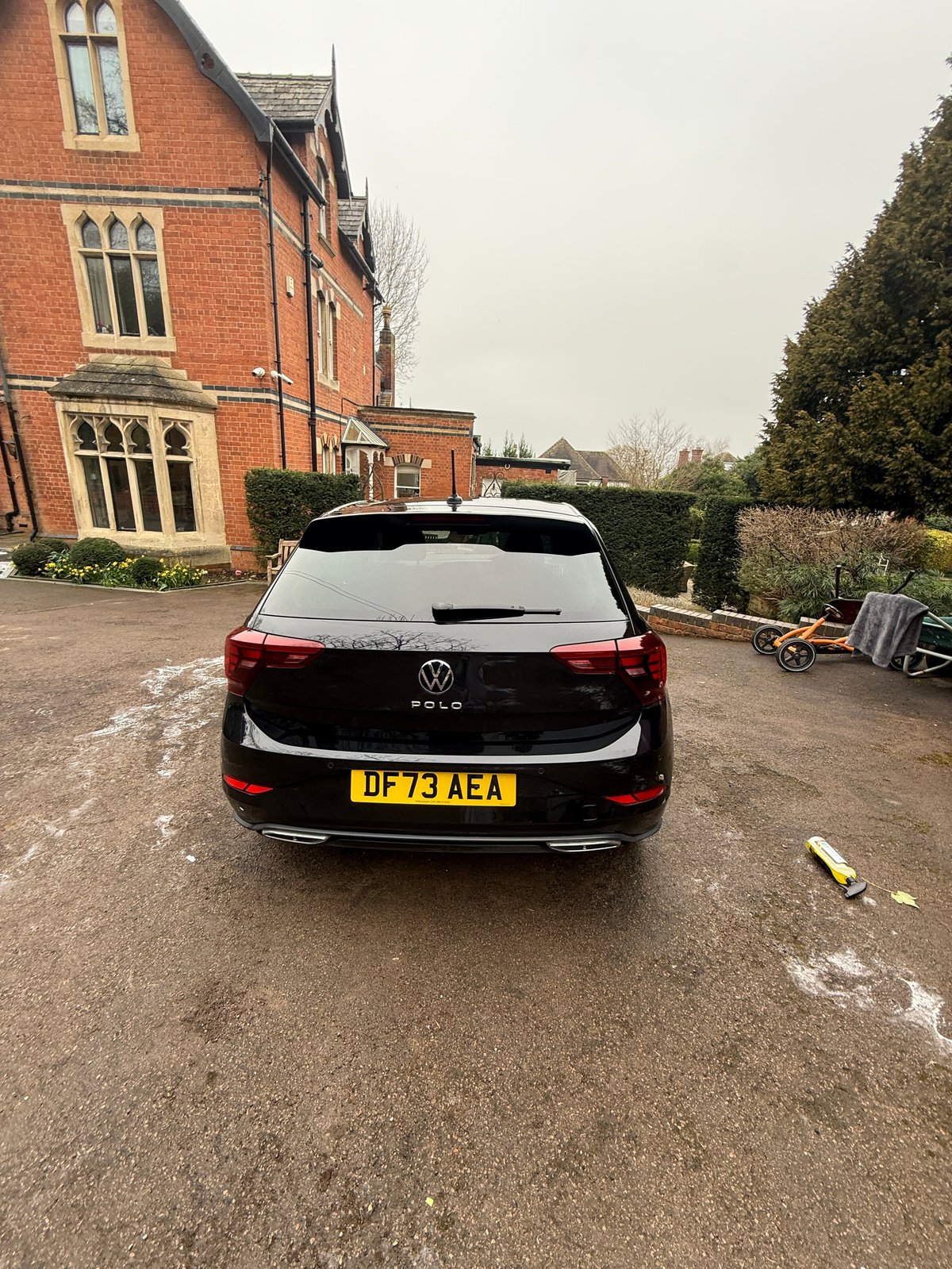 Black Volkswagen car parked on driveway in front of brick mansion with UK license plate