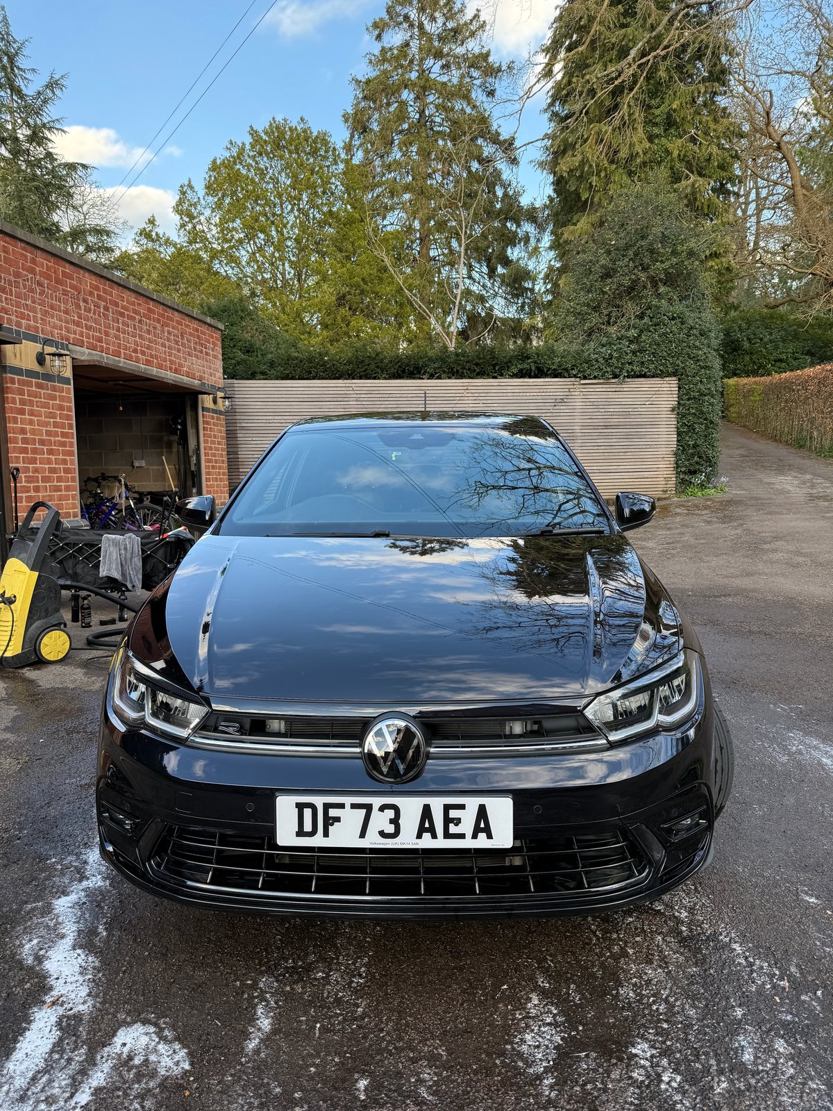 Black Volkswagen Golf parked on driveway outside brick garage with trees in background