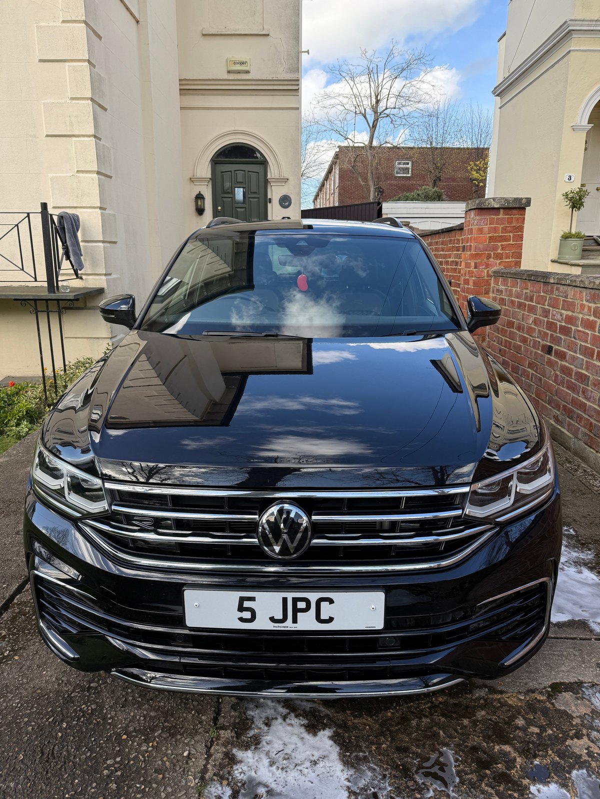Black Volkswagen car parked on driveway in front of residential properties with cream-colored stone buildings