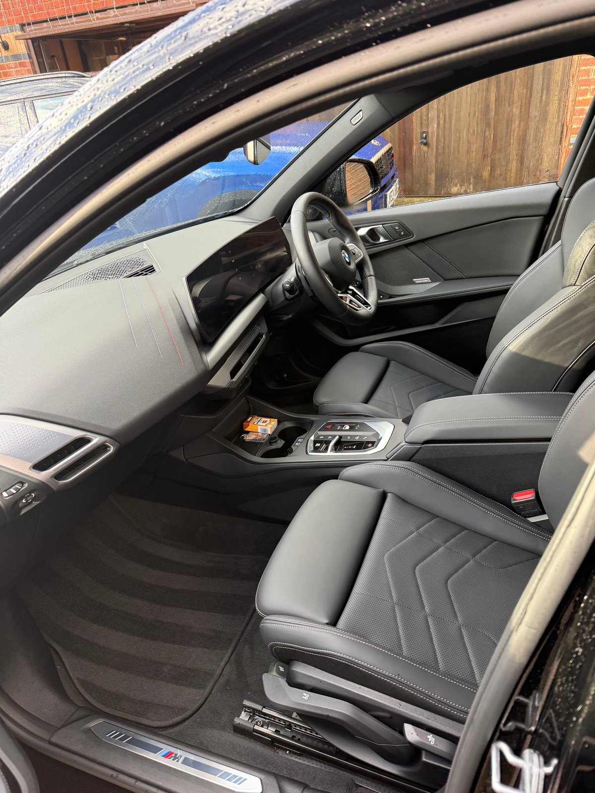 Interior view of a modern sports car with gray leather seats, steering wheel, and dashboard visible through open door