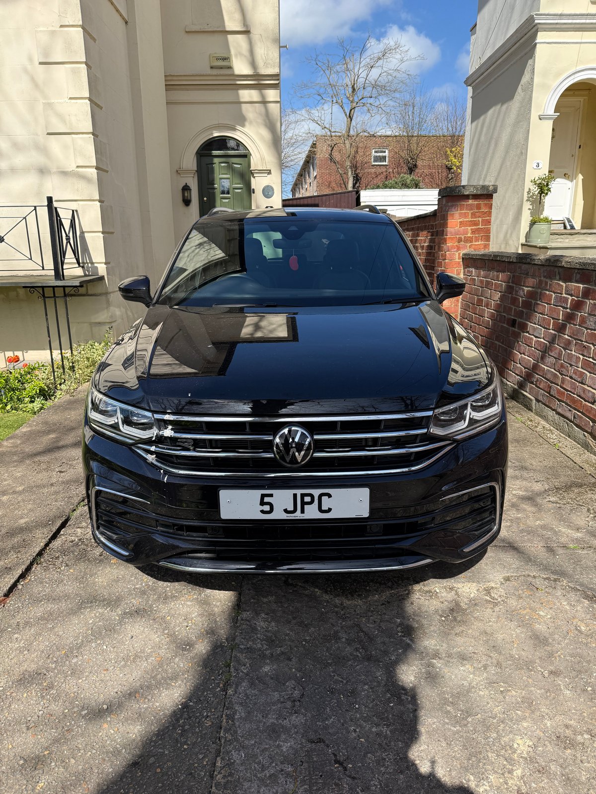 Black Volkswagen Tiguan SUV parked in driveway with license plate 5 JPC, cream-colored buildings visible in background